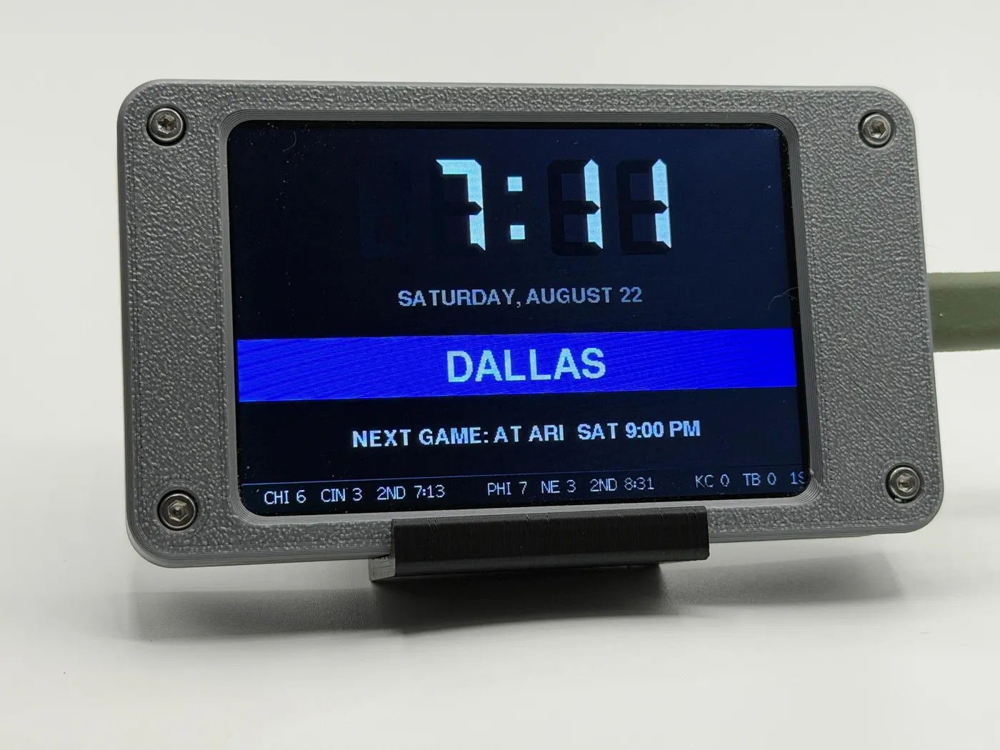 The Face: a big clock and the date, the chosen club’s city on a band across the middle, the next game named underneath, and a league score ticker along the bottom